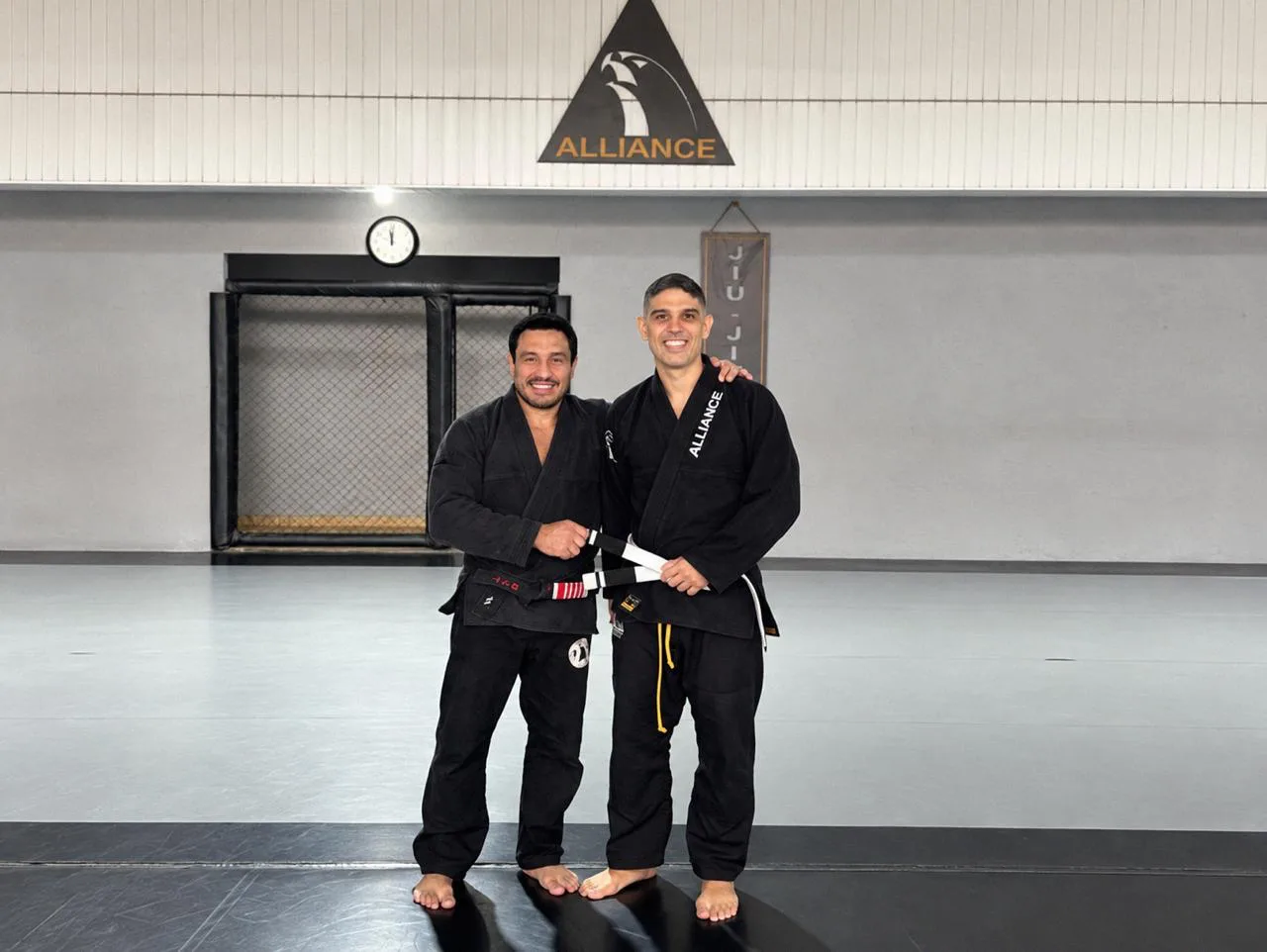Terry and his jiu-jitsu master smiling at the academy, holding a belt between them.